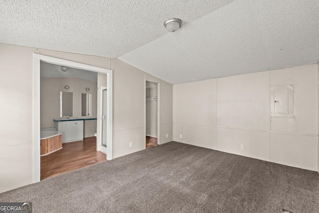 unfurnished bedroom featuring carpet, vaulted ceiling, a textured ceiling, electric panel, and a closet