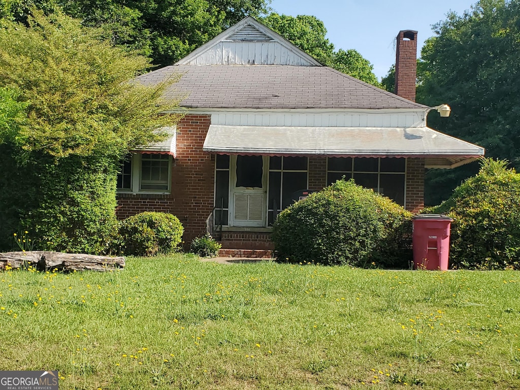bungalow-style house with a front yard, a chimney, brick siding, and roof with shingles
