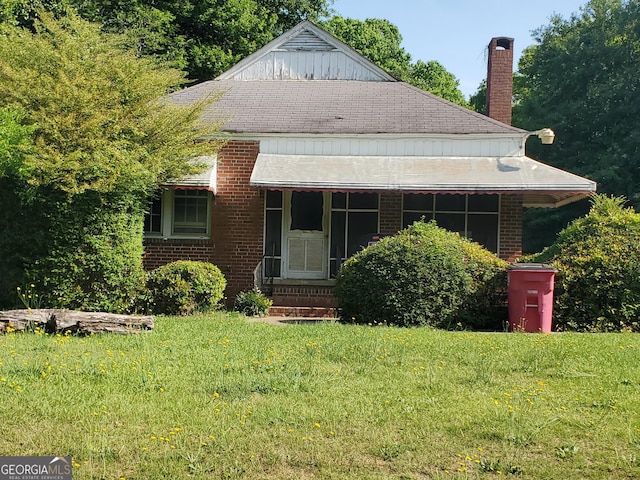 bungalow-style house with a front yard, a chimney, brick siding, and roof with shingles