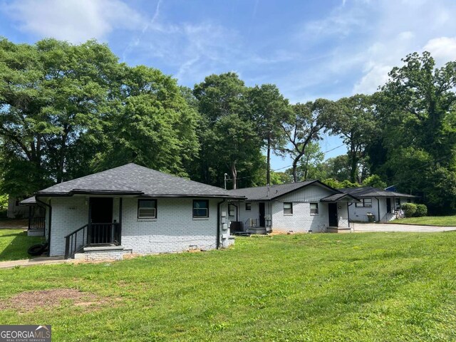 single story home featuring brick siding, a front lawn, and roof with shingles