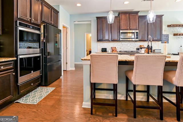 kitchen with stainless steel appliances, backsplash, dark brown cabinets, light stone countertops, and baseboards