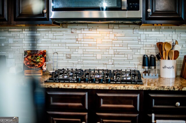 kitchen featuring stainless steel microwave, black gas cooktop, tasteful backsplash, and light stone countertops