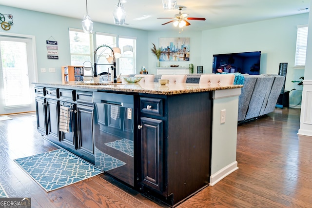 kitchen with dark wood-style floors, dishwashing machine, decorative light fixtures, open floor plan, and light stone countertops