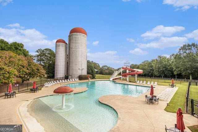 community pool featuring a water slide, fence, and a patio