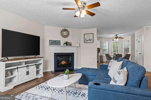 26 Springbottom Dr, Lawrenceville, GA 30046 - living room with ceiling fan, a textured ceiling, dark wood-style floors, a glass covered fireplace, and baseboards