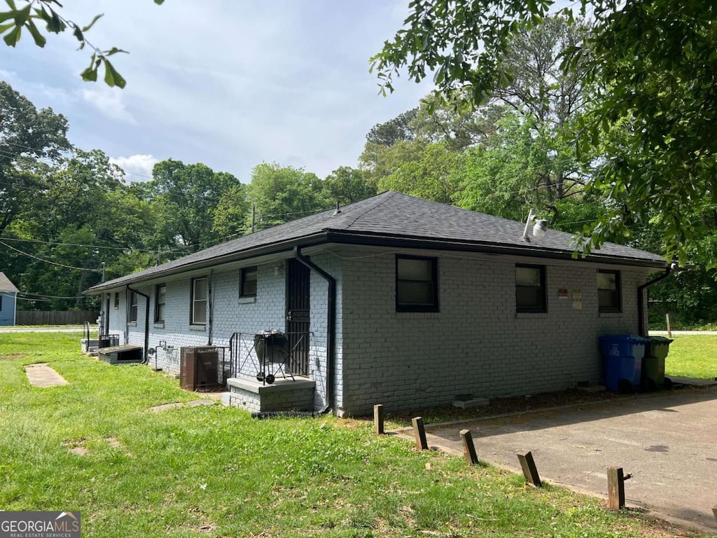 view of side of property featuring brick siding, a lawn, cooling unit, and roof with shingles