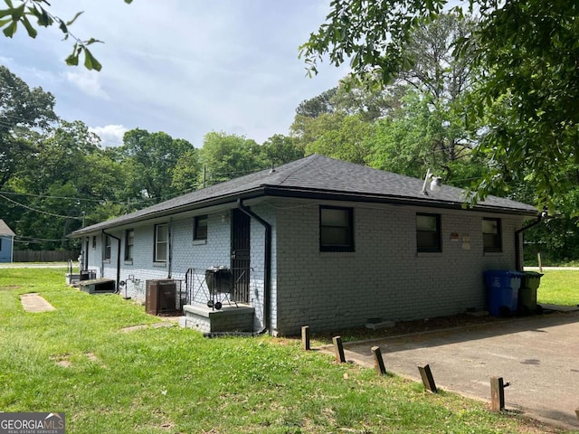 view of side of property featuring brick siding, a lawn, cooling unit, and roof with shingles