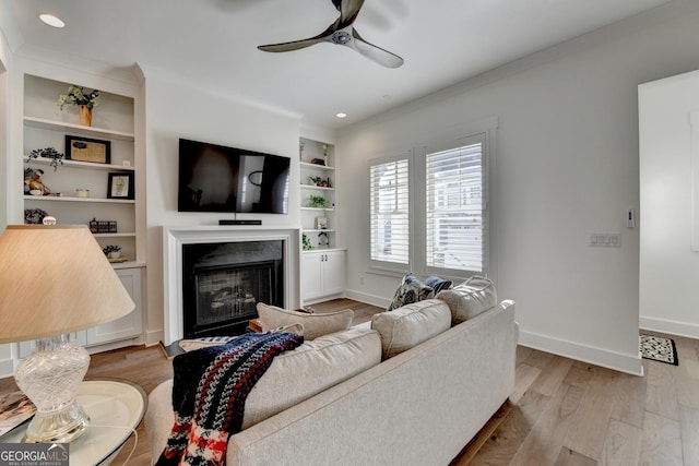 living room with a ceiling fan, light wood-style flooring, crown molding, baseboards, and a fireplace