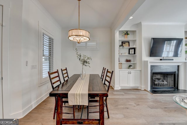 dining room featuring ornamental molding, light wood-style floors, built in features, a premium fireplace, and baseboards