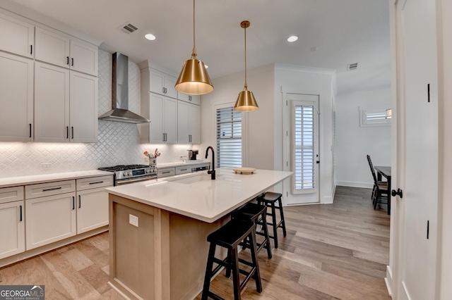 kitchen with wall chimney range hood, a sink, decorative backsplash, a kitchen bar, and light wood-style floors