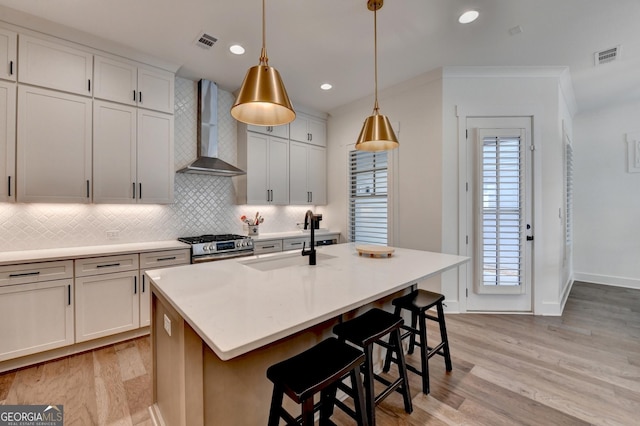 kitchen featuring wall chimney range hood, a sink, tasteful backsplash, light wood-style flooring, and recessed lighting