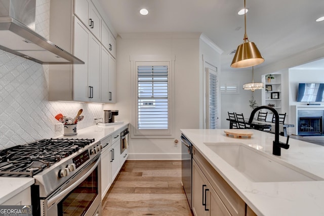 kitchen featuring appliances with stainless steel finishes, wall chimney exhaust hood, a sink, light wood-style floors, and light stone countertops