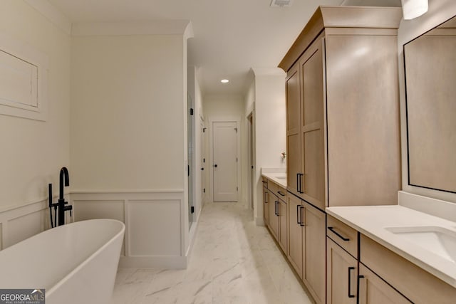full bathroom with marble look tiles, a freestanding bath, two vanities, a wainscoted wall, and recessed lighting