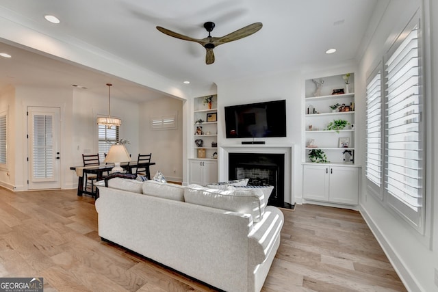 living area with light wood finished floors, ceiling fan, baseboards, built in shelves, and recessed lighting