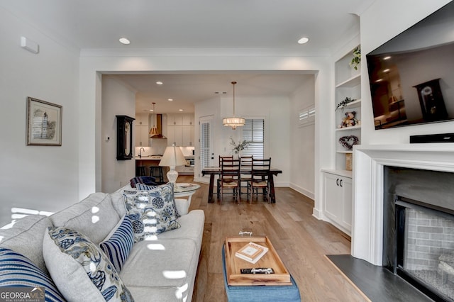 living area featuring light wood-type flooring, a fireplace, crown molding, baseboards, and recessed lighting