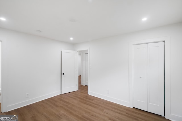 unfurnished bedroom with wood finished floors, recessed lighting, baseboards, and a closet