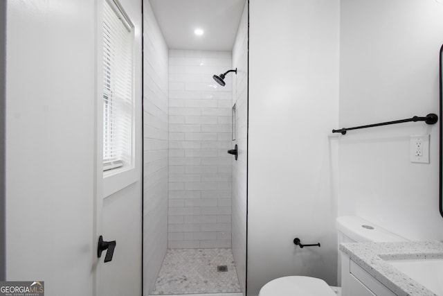 bathroom with a tile shower, toilet, and vanity