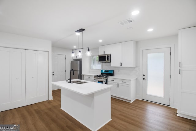 kitchen with appliances with stainless steel finishes, a sink, white cabinets, a center island with sink, and decorative backsplash