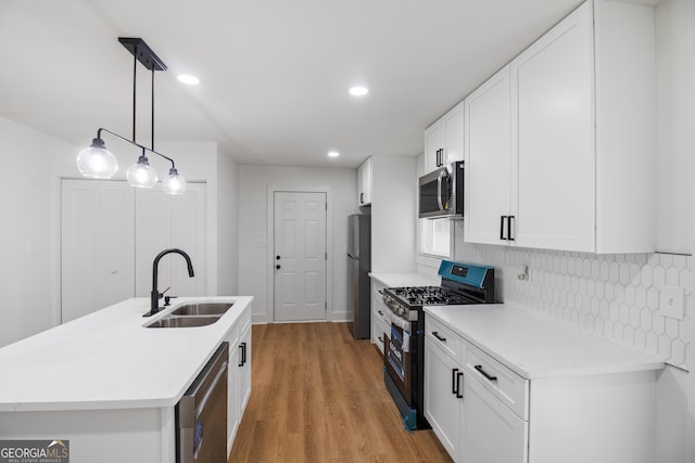 kitchen featuring appliances with stainless steel finishes, a sink, backsplash, light wood-type flooring, and white cabinets