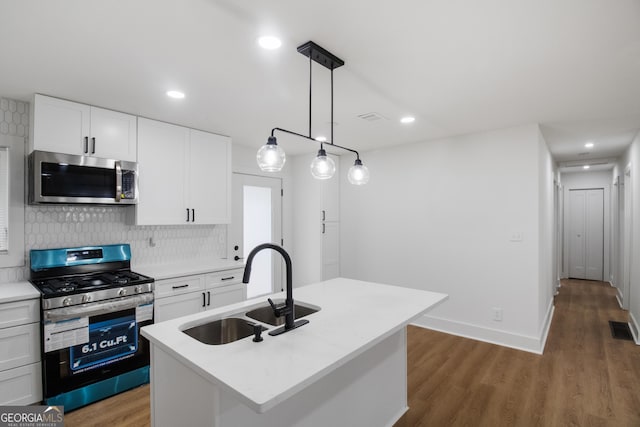 kitchen with stainless steel appliances, a sink, wood finished floors, tasteful backsplash, and white cabinetry