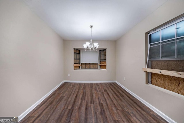 empty room featuring a chandelier, wood finished floors, and baseboards