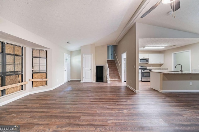 unfurnished living room with a textured ceiling, a sink, lofted ceiling, dark wood-style floors, and baseboards