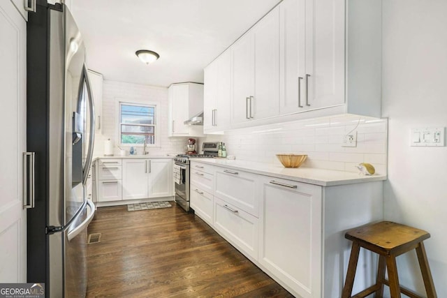 kitchen with appliances with stainless steel finishes, a sink, light countertops, white cabinets, and decorative backsplash