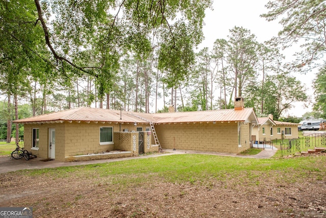 back of house with a chimney, metal roof, concrete block siding, and a lawn