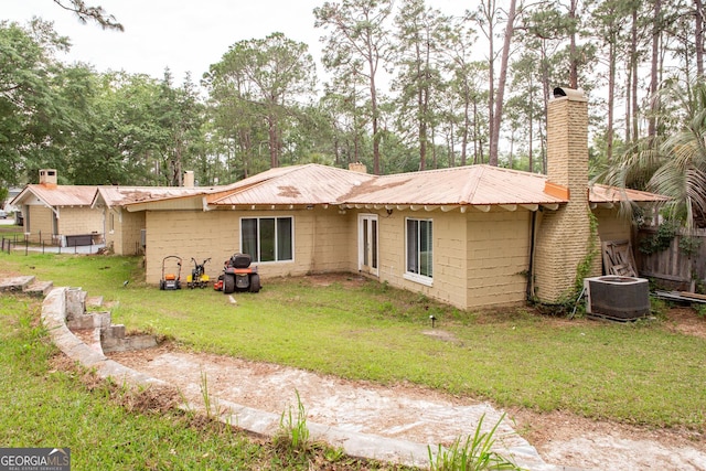 back of property with a chimney, central air condition unit, metal roof, and concrete block siding