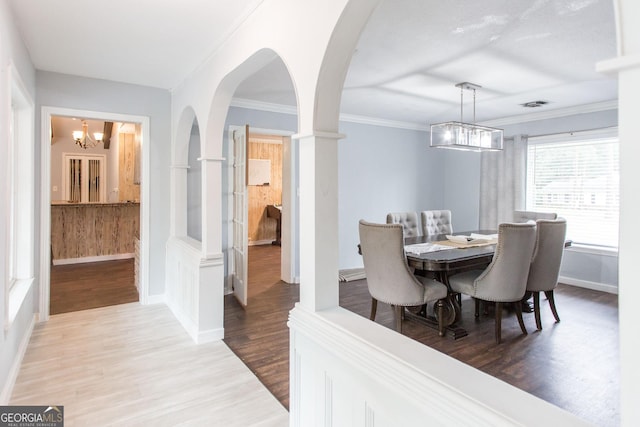 dining area featuring a chandelier, wood finished floors, arched walkways, baseboards, and crown molding