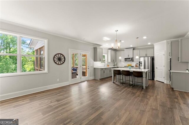 kitchen with gray cabinetry, appliances with stainless steel finishes, a kitchen island, ornamental molding, and light countertops