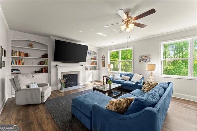living area featuring crown molding, wood finished floors, a ceiling fan, baseboards, and a fireplace with flush hearth