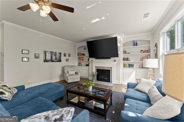 living area featuring ceiling fan, wood finished floors, baseboards, a fireplace with flush hearth, and ornamental molding
