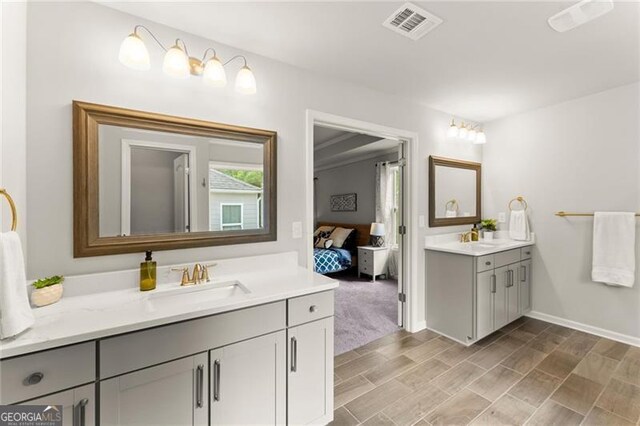 ensuite bathroom featuring two vanities, baseboards, and wood finished floors