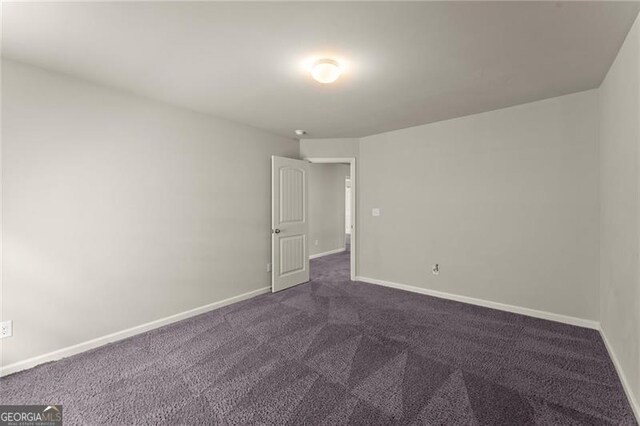empty room featuring baseboards and dark carpet