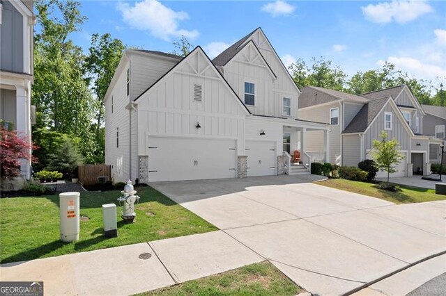 view of front of home featuring board and batten siding, driveway, stone siding, a front yard, and an attached garage