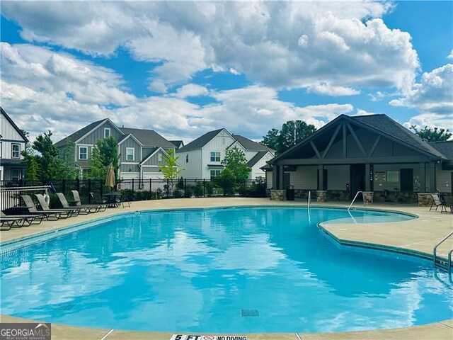 community pool with a patio, fence, and a residential view