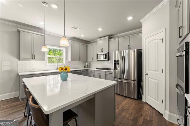 kitchen with stainless steel appliances, gray cabinets, a breakfast bar area, tasteful backsplash, and ornamental molding
