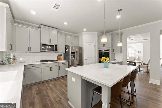 kitchen featuring stainless steel appliances, ornamental molding, a kitchen island, decorative backsplash, and dark wood-style flooring