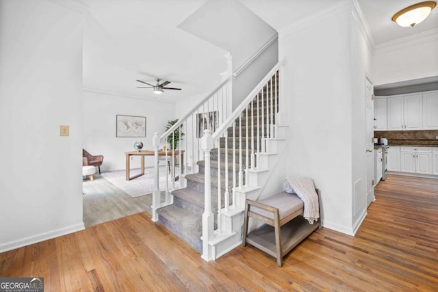stairs featuring a ceiling fan, wood finished floors, crown molding, and baseboards