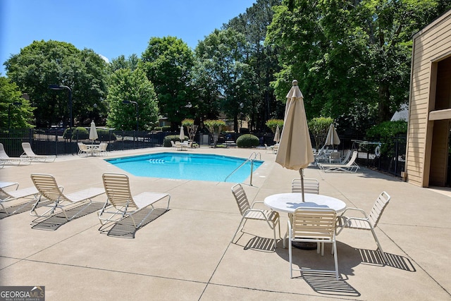 community pool with fence, a patio, and view of wooded area