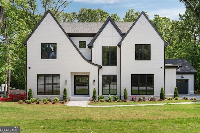 modern farmhouse featuring board and batten siding, a front yard, brick siding, an attached garage, and a shingled roof