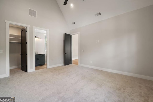 unfurnished bedroom with a spacious closet, light colored carpet, high vaulted ceiling, baseboards, and a closet