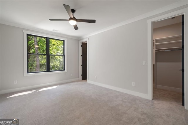 unfurnished bedroom featuring ornamental molding, a walk in closet, carpet flooring, baseboards, and a closet