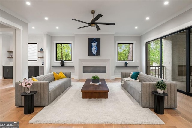 living area featuring a glass covered fireplace, ornamental molding, recessed lighting, light wood-style floors, and a ceiling fan