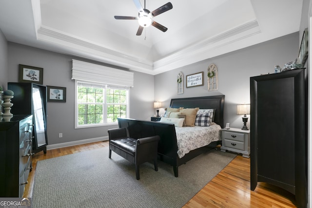 bedroom featuring a tray ceiling, wood finished floors, ornamental molding, baseboards, and ceiling fan