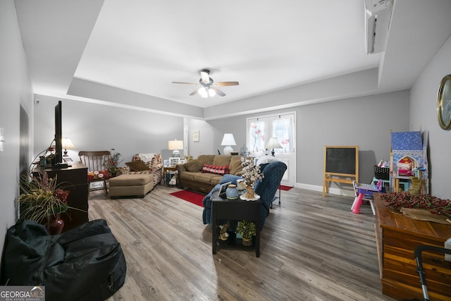 living room featuring a ceiling fan, wood finished floors, baseboards, and a tray ceiling