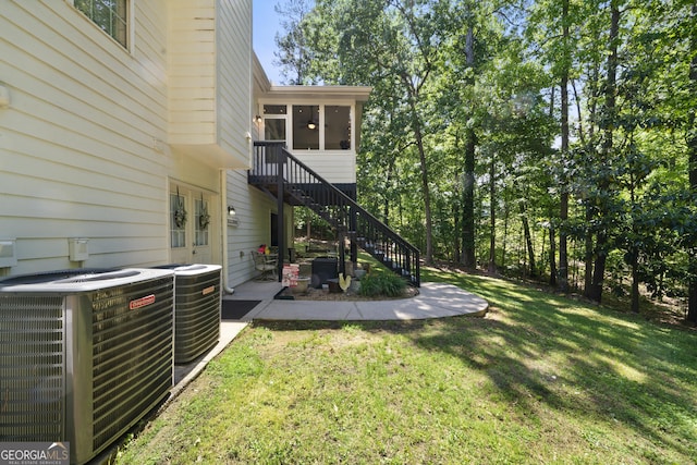view of grassy yard with central air condition unit, stairs, and a sunroom