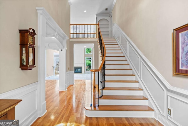 stairs featuring a decorative wall, arched walkways, a wainscoted wall, wood finished floors, and a high ceiling
