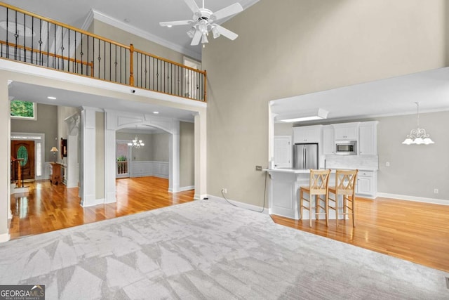 unfurnished living room featuring a towering ceiling, a chandelier, light wood-type flooring, light colored carpet, and arched walkways